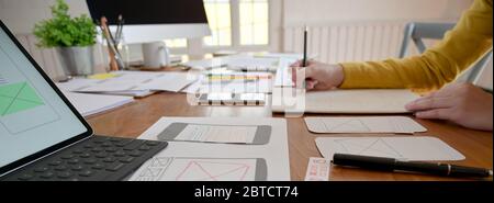 Side view of UI developer working on wooden table with notebook, paperwork and computer Stock Photo