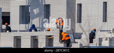 Construction site. Unfinished apartment building. Construction workers dressed in special clothing laying bricks. Stock Photo
