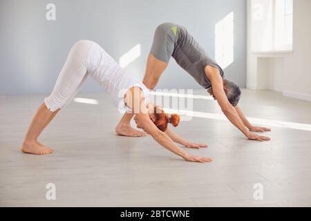 Middle aged man and woman standing in dog position while practicing yoga together in light workout room Stock Photo