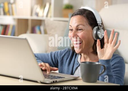 Happy adult woman videocalling with headphones on laptop webcam sitting on the floor at home Stock Photo