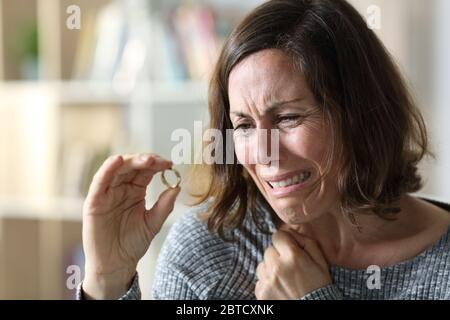 Sad adult wife crying complaining looking at wedding ring sitting at home Stock Photo