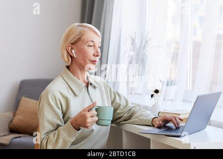 Mature woman working at home she drinking coffee and typing on laptop computer Stock Photo