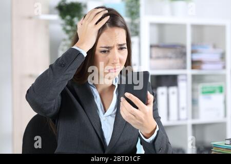Sad worried executive woman discovers mistake on smart phone sitting on a desk at office Stock Photo