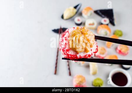 Close up of chopsticks taking portion of sushi roll above table with assorted sushi, soy sauce, ginger, wasabi. Sushi menu. Delivery service Japanese Stock Photo