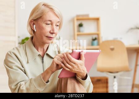 Mature serious woman using digital tablet at home she typing on the digital screen and listening to music Stock Photo