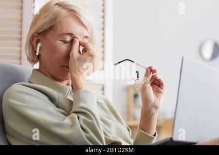 Mature woman sitting on armchair and resting she holding her head with hands she tired of work Stock Photo