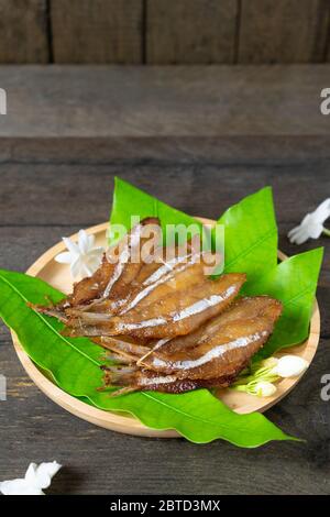 Fried dried fish on mango leaf in wooden dish on wooden table. Stock Photo