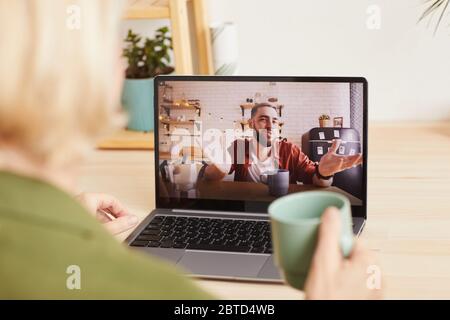 Young man on computer monitor talking online with woman who sitting at the table with cup of coffee Stock Photo