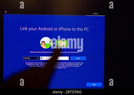 London, United Kingdom - Mar 28, 2020: Man selecting Link your Android or iPhone to this PC hand POV touching the touchscreen of a modern Microsoft Windows PC computer during the update Stock Photo