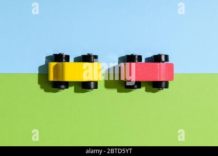 Two colorful yellow and red wooden toy cars on a split green and blue background viewed from the top down with shadows Stock Photo