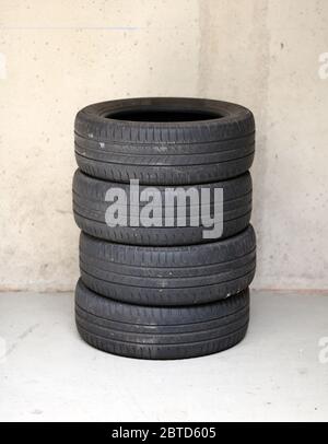 Set of four stacked used car or motor vehicle tires on a concrete floor against a wall with copy space Stock Photo