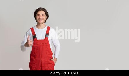 Handyman Services Concept. Smiling Young Workman In Uniform Showing Thumb Up Stock Photo