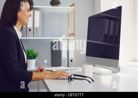 Work online using a computer. Business woman in a black business suit sitting at the workplace works with the computer in the office at home. Remote v Stock Photo