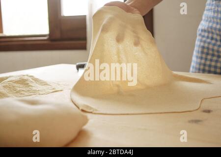 Making homemade fresh pasta: backlit woman hand show the transparency of the just rolled out fresh pasta, traditional Italian pasta, the woman cooks t Stock Photo
