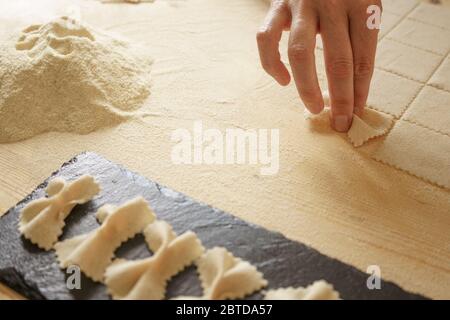 Close up detail of process of homemade vegan farfalle pasta with durum wheat flour. The cook kneads the dough on the wooden cutting board, traditional Stock Photo