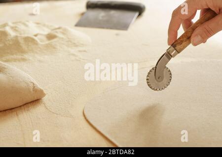 Close up process of homemade vegan farfalle pasta with durum wheat flour. The cook uses the rolling cutter to cut the dough, traditional Italian pasta Stock Photo