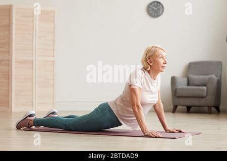 Senior woman doing stretching exercises on the floor in the room at home Stock Photo