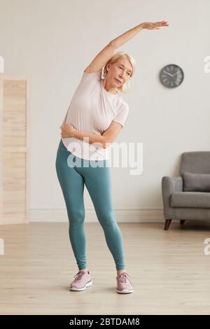 Senior woman standing and doing morning exercises in the room at home Stock Photo