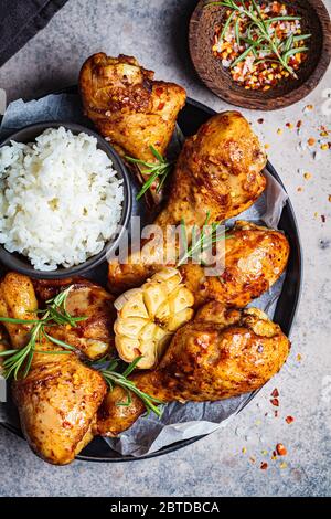 Fried spicy chicken legs with rice, garlic and herbs in a black plate, dark background. Stock Photo