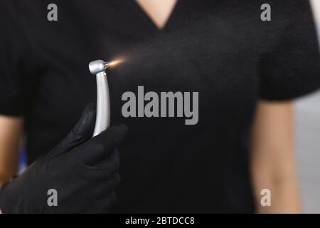 Unrecognizable doctor in black scrubs and latex glove carrying dental drill during work in modern clinic Stock Photo