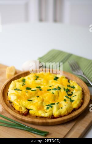 Fluffy omelette from whipped eggs with cheddar cheese and green onion scallions sprinkled on it in a wooden plate. Stock Photo