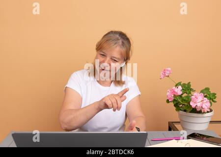Happy middle age woman in headphones speaking looking at laptop, elderly student talking by video conference call, female teacher trainer tutoring by Stock Photo