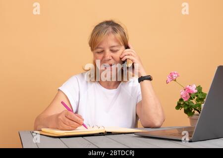 Smiling middle age woman talking on phone, sitting at home, attractive female holding smartphone, making or answering call, having pleasant Stock Photo