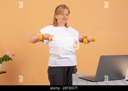 Woman using laptop at home watching fitness videos online workout class training with yellow dumbbells Stock Photo