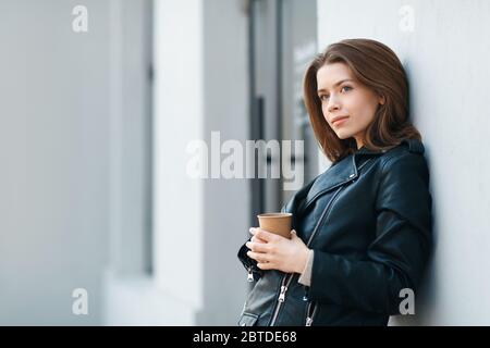 Happy casual brunette female staying near grey wall with coffee Stock Photo