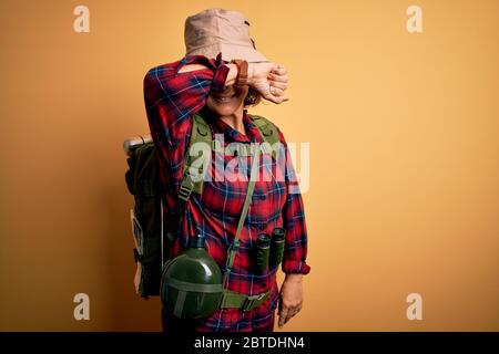 Middle age curly hair hiker woman hiking wearing backpack and water canteen using binoculars Smiling cheerful playing peek a boo with hands showing fa Stock Photo