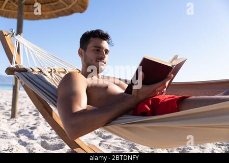 Caucasian man lying on a hammock and reading a book at the beach. Stock Photo