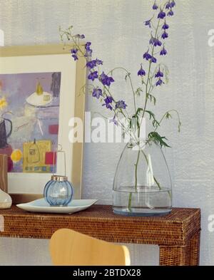 Spray of blue delphiniums in glass vase on wicker console Stock Photo