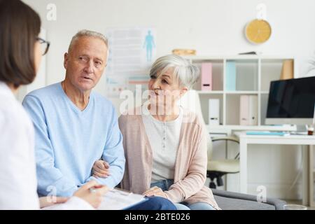 Portrait of modern senior couple listening to female doctor while visiting clinic, copy space Stock Photo