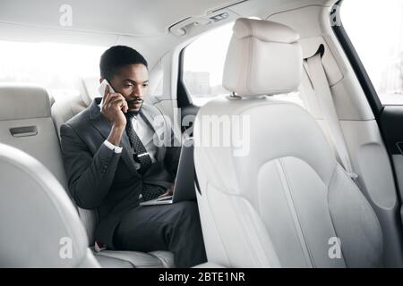Serious Businessman Working On Laptop, Talking On Cellphone In Car Stock Photo