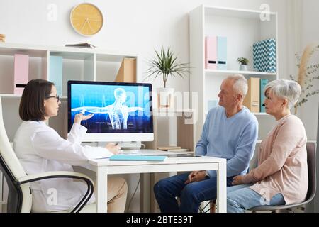 Portrait of modern senior couple listening to female doctor and looking at x-ray image during consultation in clinic Stock Photo