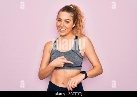 Young beautiful blonde sportswoman with blue eyes doing exercise wearing sportswear In hurry pointing to watch time, impatience, upset and angry for d Stock Photo