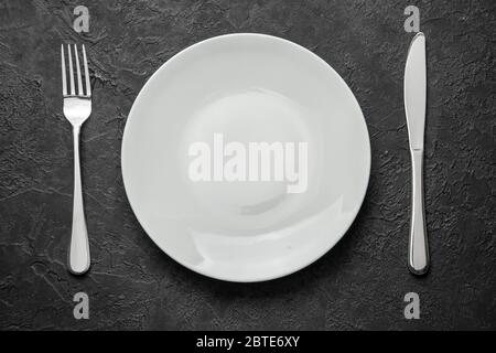 Empty white plate with knife and fork on black table Stock Photo