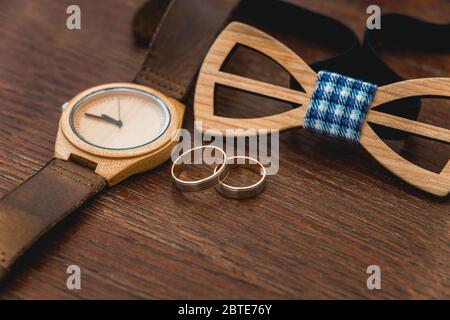 Stylish wooden watch and bow tie for groom on a table in hotel room. Morning preparation before wedding ceremony. Men accessory for luxury event. Stock Photo