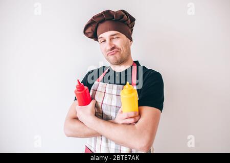 Young man isolated over white background. Positive confident professional cook posing on camera with ketchup and mustard in hands Stock Photo