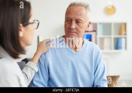 Portrait of young female psychologist consulting senior man during therapy session in clinic or office Stock Photo