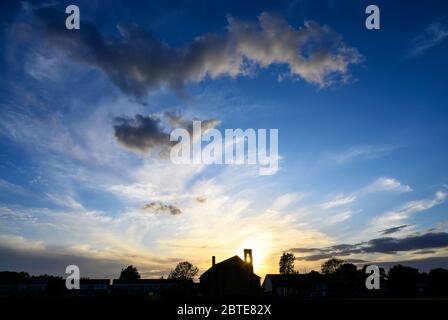Dramatic clouds at sunset over St Johns Church in Beckenham, Kent, UK. The setting sun shines through the bell tower of the church with beautiful sky. Stock Photo