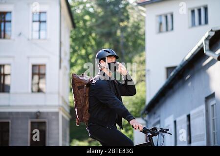 Delivery man courier on bicycle with face mask and smartphone delivering in town. Stock Photo