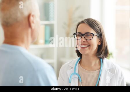 Head and shoulders portrait of smiling female doctor shaking hands with senior patient while standing in clinic interior Stock Photo