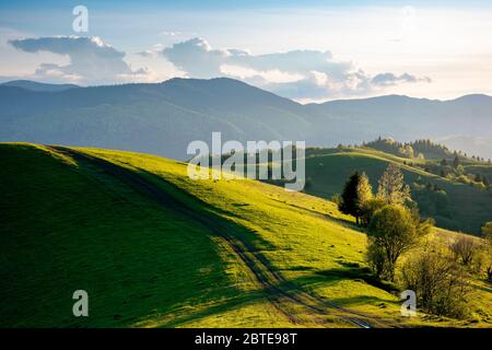 path through countryside fields. beautiful view of rural landscape at sunset. hills rolling down in to the distant valley. clouds on the blue sky in e Stock Photo