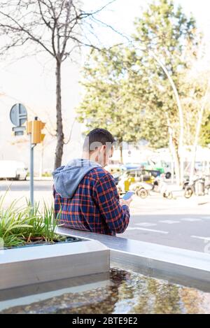 Rear view of a fashion cool urban bearded man with smartphone on city street. Stock Photo