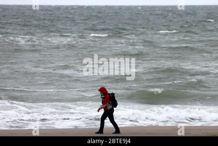 Mecklenburg, Germany. 25th May, 2020. 25 May 2020, Mecklenburg-Western Pomerania, Warnemünde: Wind and clouds make for grey dirty weather at the Baltic Sea, a woman goes for a walk alone on the beach. Photo: Bernd Wüstneck/dpa-Zentralbild/dpa Credit: dpa picture alliance/Alamy Live News Stock Photo