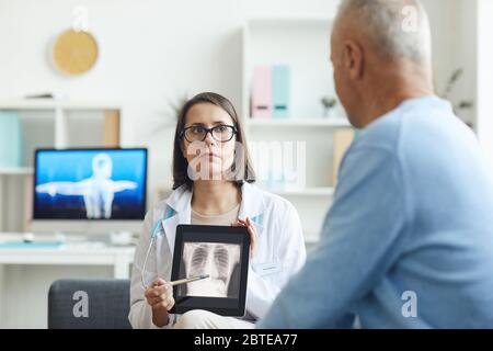Portrait of serious female doctor holding x-ray image of lungs and chest while consulting senior patient in clinic, copy space Stock Photo