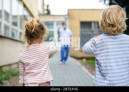 Children waving at father doctor in front of hospital, coronovirus and isolation concept. Stock Photo