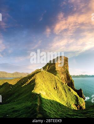 Incredible sunset landscape with Kallur lighthouse on green hills of Kalsoy island, Faroe islands, Denmark Stock Photo