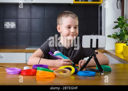 Child creating with 3d printing pen. Happy boy does something with colored ABS plastic and using online lesson. Creative hobby at home, technology, le Stock Photo